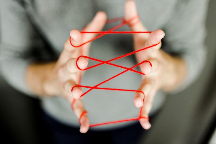 Hands show playing cat's cradle with red wool